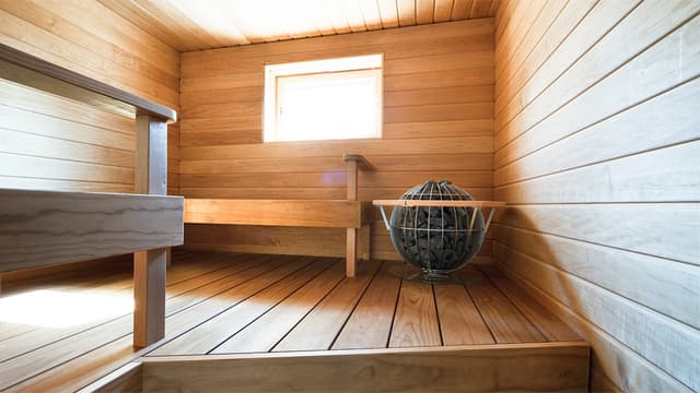 Vaaleasta puupaneelista ja laudetavarasta tehty sauna, jonka nurkassa pyöreä kiuas.