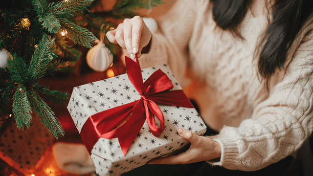 henkilö avaa joulupakettia kuusen juurella