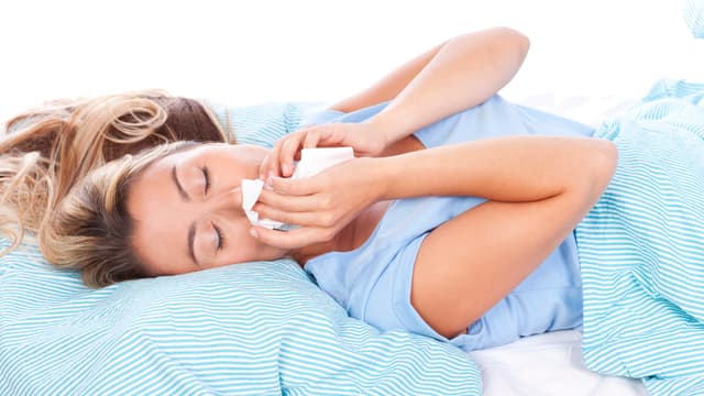 Nainen makaa sängyssä ja niistää