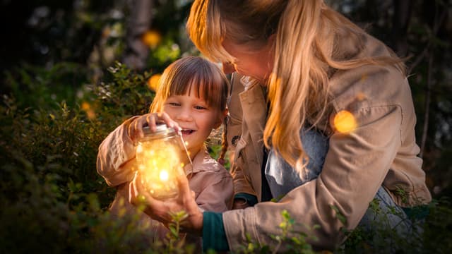 Nainen ja lapsi metsässä, naisella kädessään purkki, jossa hehkuu valoa