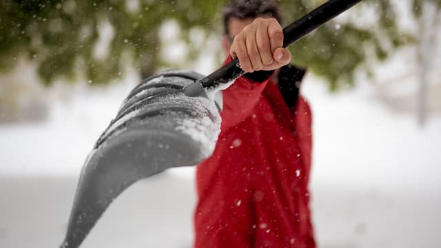 Punaiseen takkiin pukeutunut mies pitää lumilapiota edessään