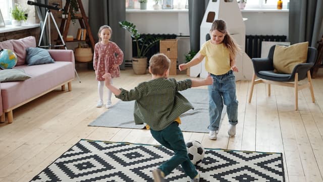 iloiset lapset leikkivät sisällä olohuoneessa jalkapallolla