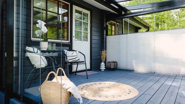 Tumman talon oven eteen on asennettu terassilasitus, oven vieressä kaksi tuolia.