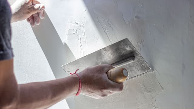 rakennusmies laittaa vaaleaa tasoitetta seinään lastan avulla