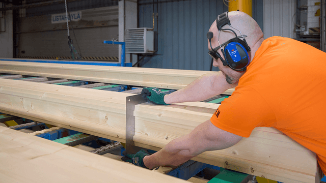 hirsitalotehtaan työntekijä tarkastaa hirren mittoja