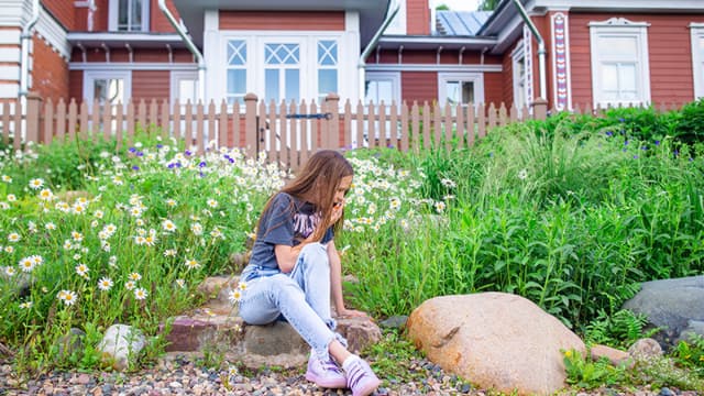 Tyttö kerää kukkia talon edustalla