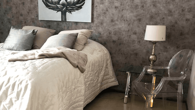 makuuhuoneessa suuri parisänky ja muovinen läpinäkyvä tuoli yöpöydän vieressä