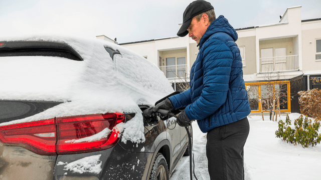 mies lataa sähköautoa lumisella pihalla